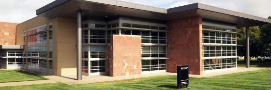 Front 3/4 view of CAER Lab 2: a brick and glass building with two stories, a grey flat roof, and large windows.